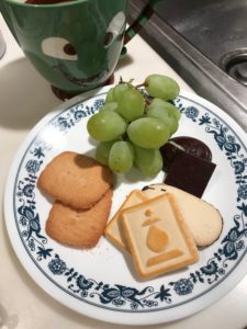A plate with cookies, chocolates and grapes next to a mug of tea