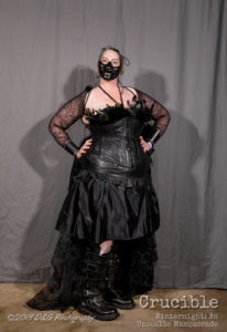 Back leather corseted dress, distressed lace sleeves and Goth leather and metal boots being worn by Miss R, A black demon mask covering the bottom half of her face.
